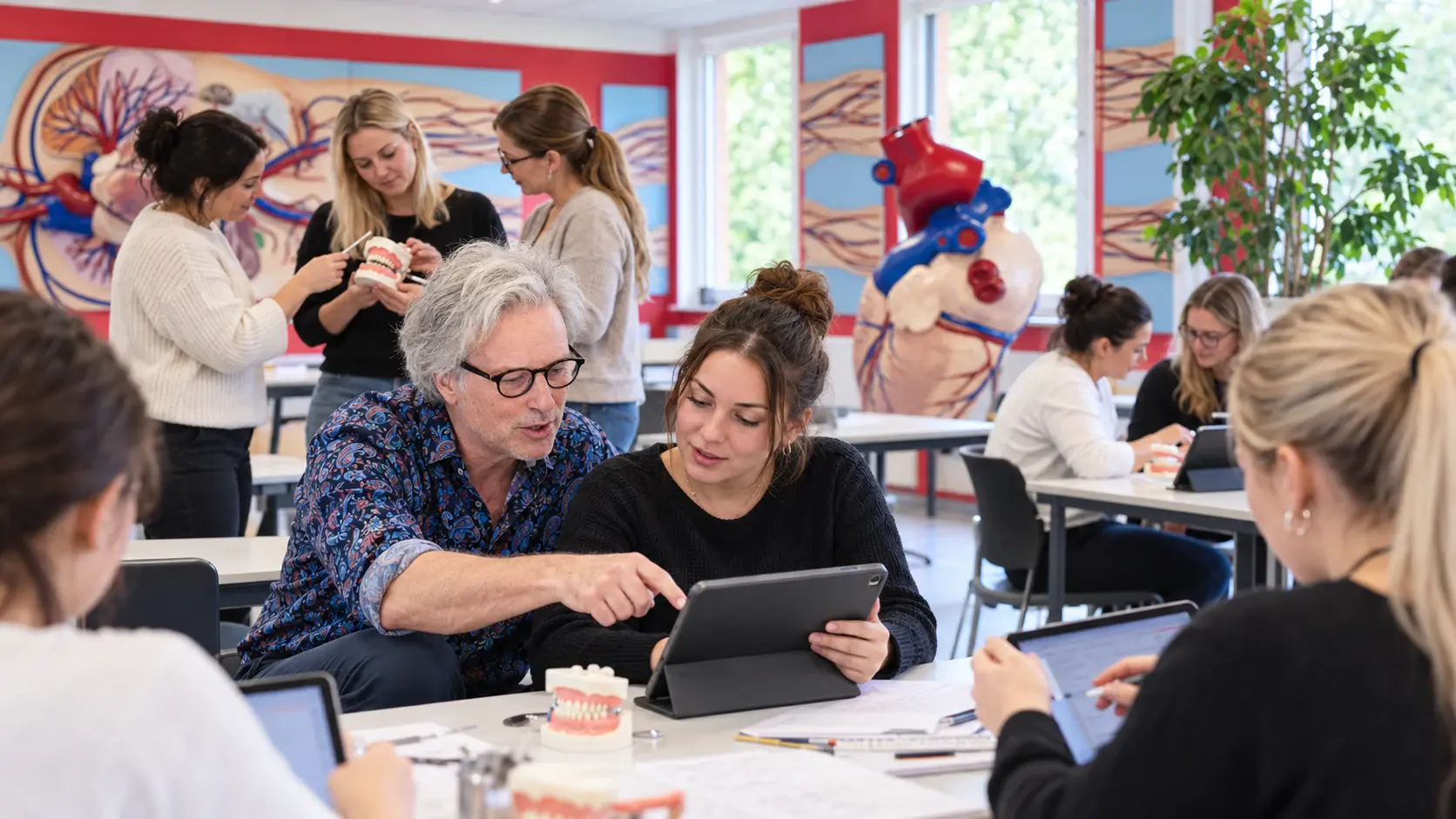 Steffen Schuster arbeitet in einem von educube gestalteten Lernraum auf Augenhöhe mit einer ZFA-Auszubildenden; weitere Lernende arbeiten mit Tablets und einem Zahnmodell.